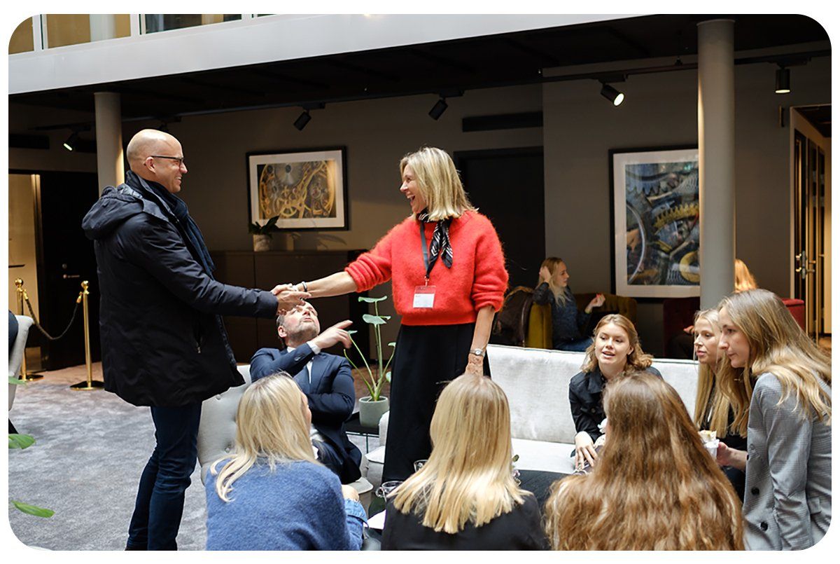 En man och en kvinna tar i hand med varandra leende och skrattandes. Bredvid sitt sju personer och nätverkar.
